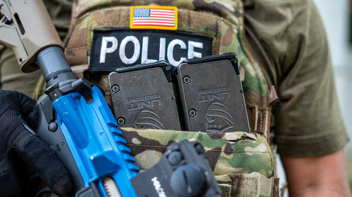 Deux chargeurs UNIT4 UNIT Solutions sur gilet tactique police — opérateur avec fusil d'entraînement bleu